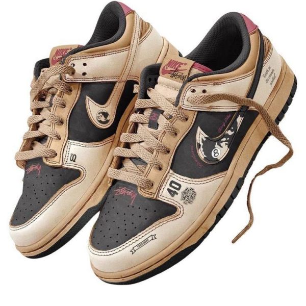 Pair of tan and black Nike sneakers with beige laces and a chunky sole, featuring graphic patches and multiple logos on the panels.