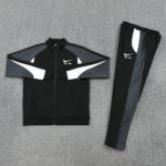 Black Nike Air tracksuit jacket and matching pants laid flat with white/gray panel accents on a gray carpeted floor.