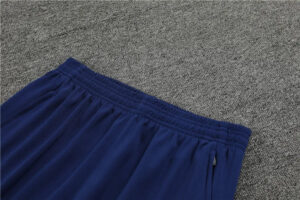 Blue elastic-waist track pants laid on a gray carpet area outside of a store.
