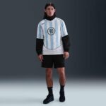 Male model in a light blue and white striped soccer jersey with number 90, black shorts, and black sneakers, standing against a gray backdrop.