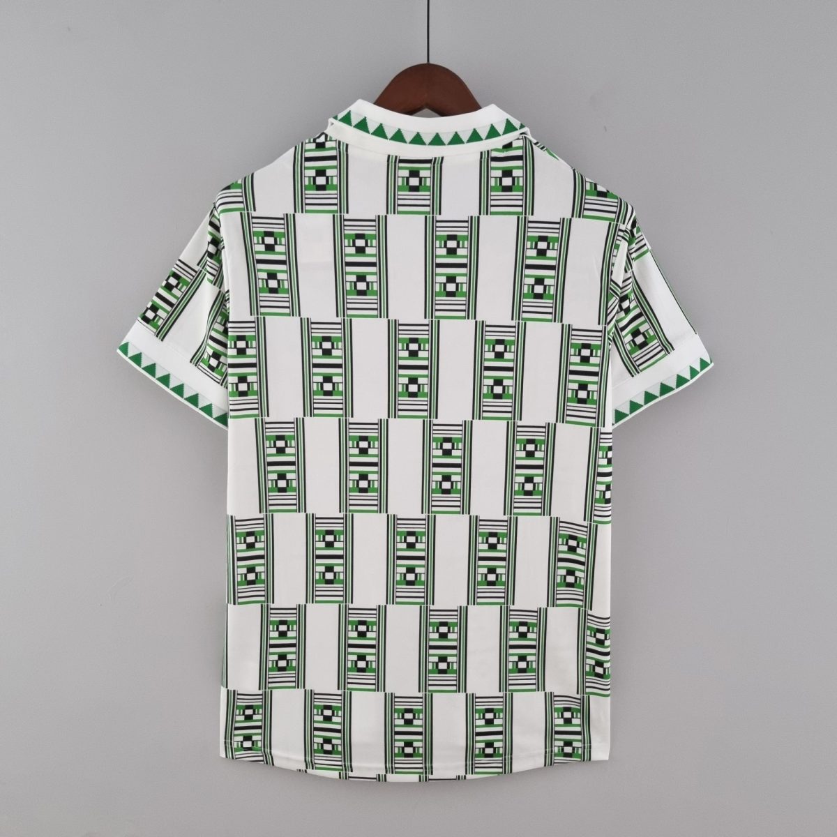 Back view of a white short-sleeve shirt on a wooden hanger, featuring a bold green and black geometric pattern against a gray background.