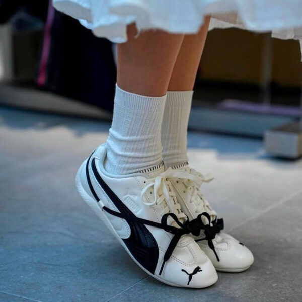 Child wearing white crew socks and white Puma sneakers with black stripes on a blue floor.