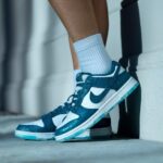 Teal and white Nike sneaker on a white sock, resting against a concrete wall.
