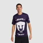 Male model wearing a dark purple graphic T-shirt with large white logo on chest and sponsor logos (DHL, Mifel) visible, against a light gray backdrop