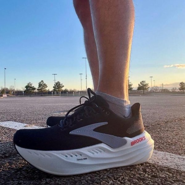 Close-up of a black Brooks running shoe with a white sole on textured pavement at sunset, worn by a person standing.