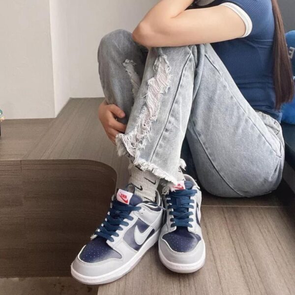 Person sitting on the floor with knees drawn up, wearing ripped light-wash jeans and blue‑and‑white Nike sneakers seen from the side/forward angle.
