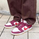 604dd3e9-5624-4795-9ed9-ea933b4e503c_8bebd231-52a7-4b33-b157-9ee9c8f6b7f8 | UAE SPORT STORE Pair of burgundy and white Nike sneakers with gum soles on a tiled pavement, worn with brown pants.
