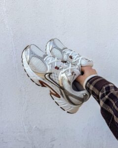 Person in a plaid sleeve holds a pair of white and gray running shoes against a pale wall.