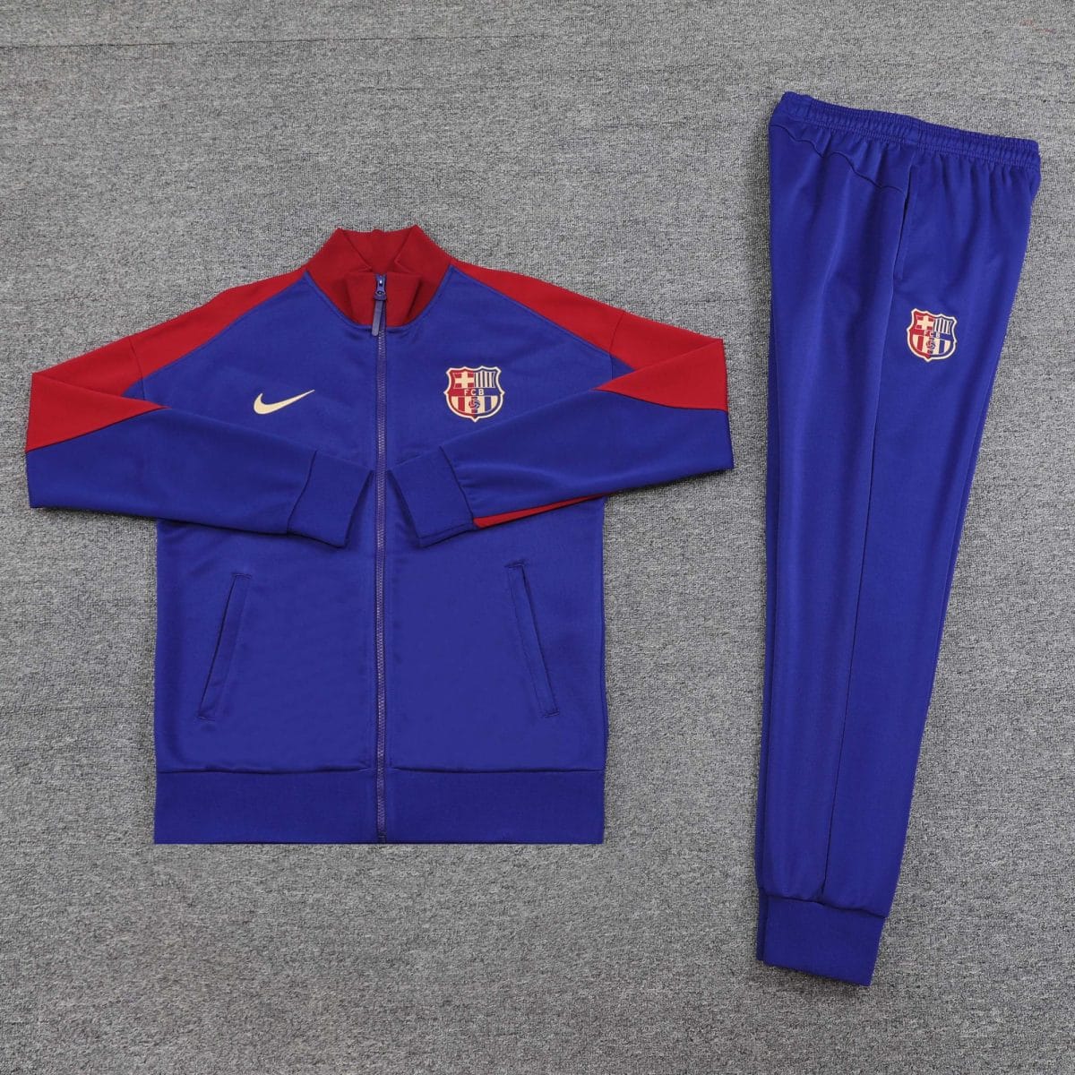 FC Barcelona blue and red tracksuit laid out on a gray carpet, jacket next to pants with club crest.