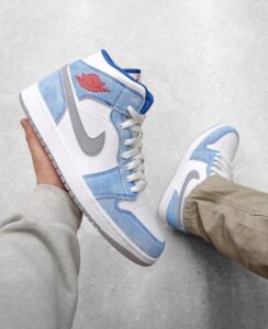 High-top white-and-light-blue sneakers with a gray Nike swoosh being held by a person, on a gray floor.