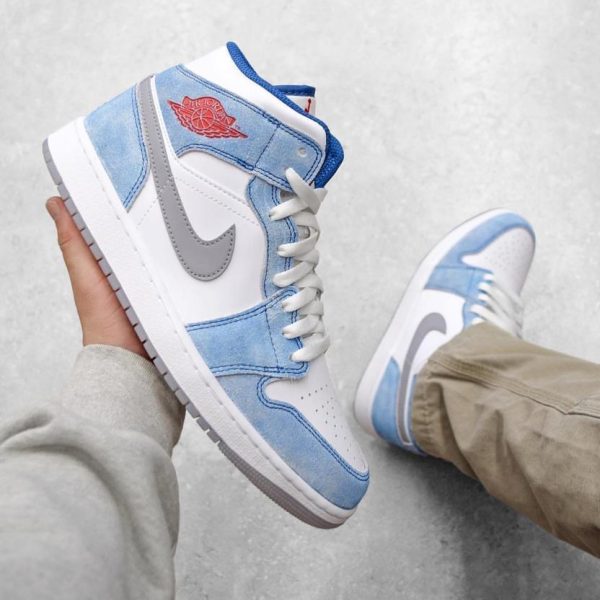 High-top white-and-light-blue sneakers with a gray Nike swoosh being held by a person, on a gray floor.
