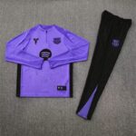 Purple Barça-style long-sleeve training top with black side panels and crest, paired with black pants featuring a purple crest on a gray carpet.