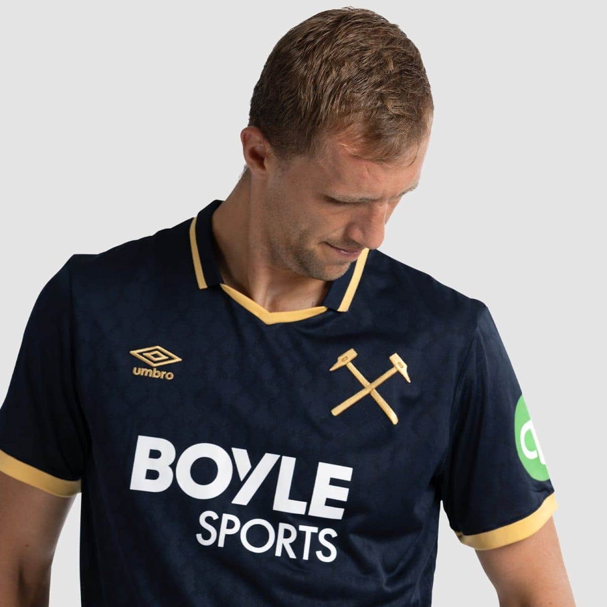 Man wearing a navy blue Boyle Sports jersey with gold trim, Umbro logo, and a crossed hammers emblem, looking down to the left.