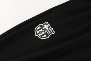 615fc694 | UAE SPORT STORE Close-up of black fabric with a small white embroidered FC Barcelona shield logo partially visible.