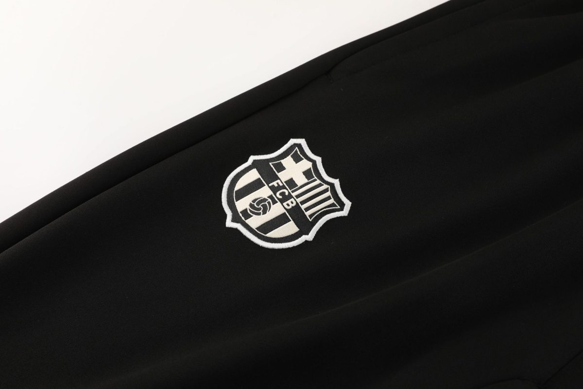 Close-up of black fabric with a small white embroidered FC Barcelona shield logo partially visible.