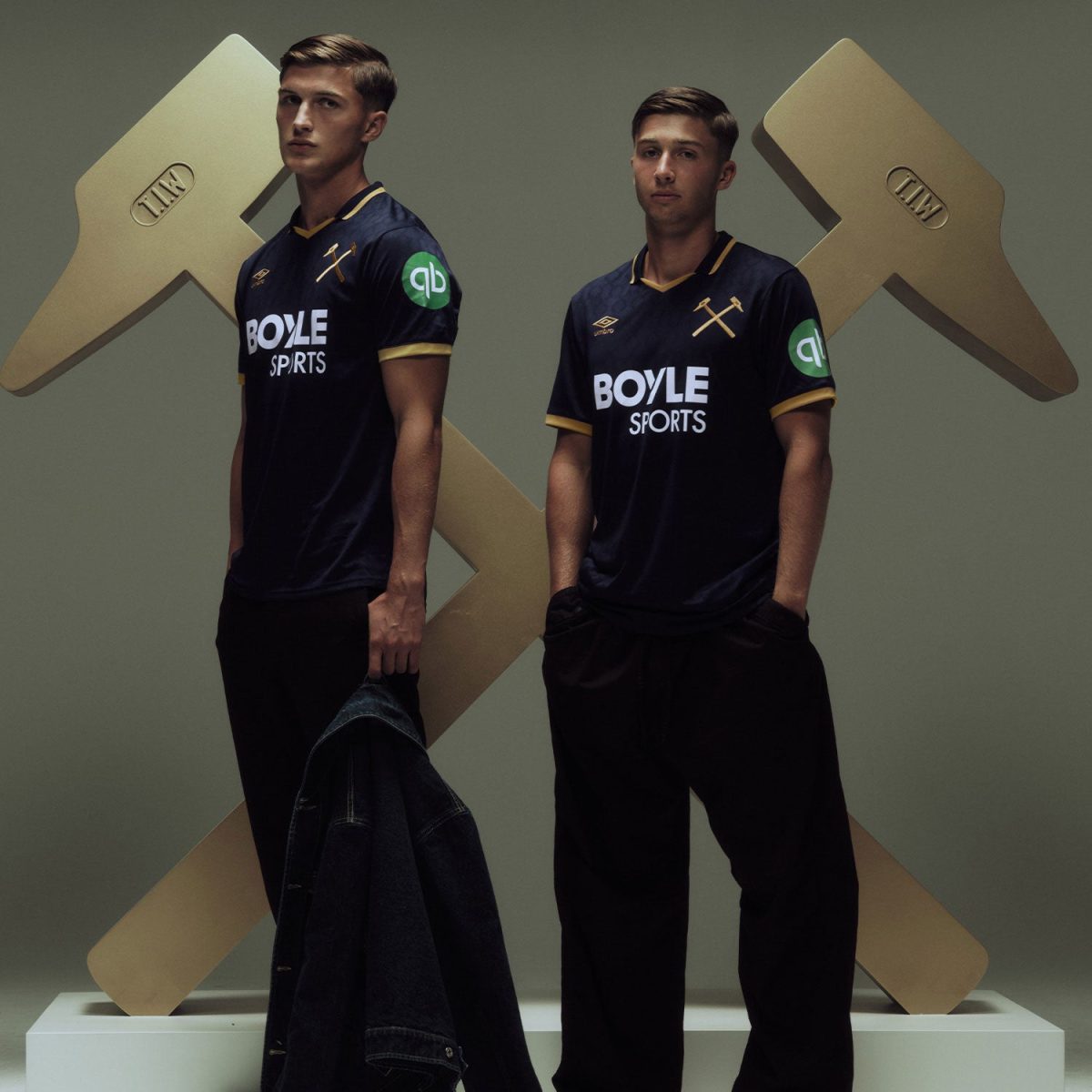 Two male models in navy jerseys with Boyle Sports logos stand side by side in front of oversized gold X-shaped props.