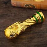 Novelty gold-toned phallic bottle stopper resting on a dark wooden surface with a book in the background.