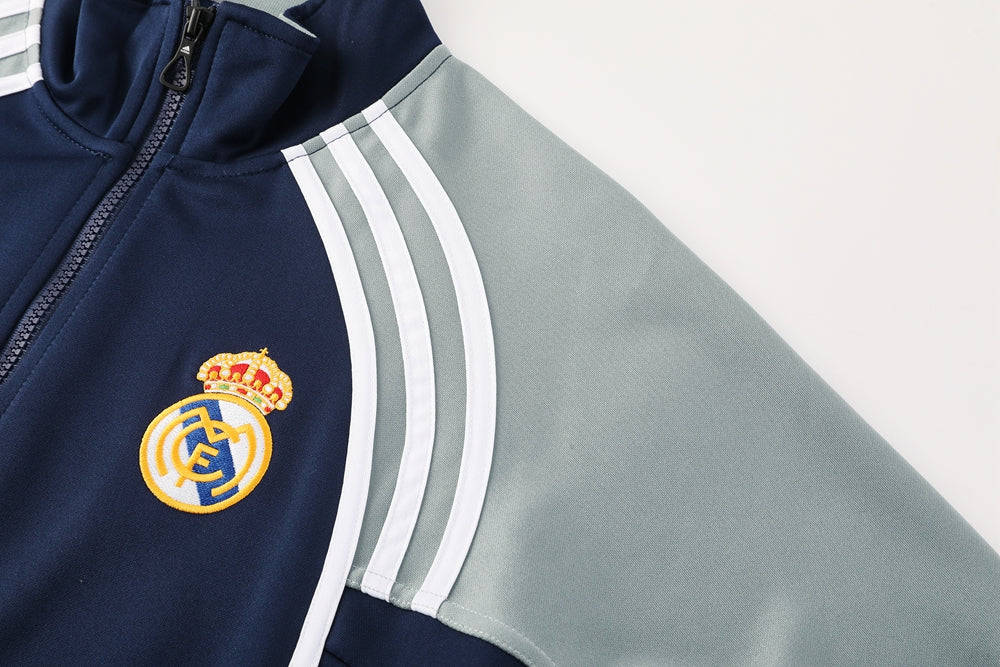 61aba6a6 | UAE SPORT STORE Close-up of a navy Real Madrid jacket with a gray sleeve, zipper, white stripes, and the club crest visible.
