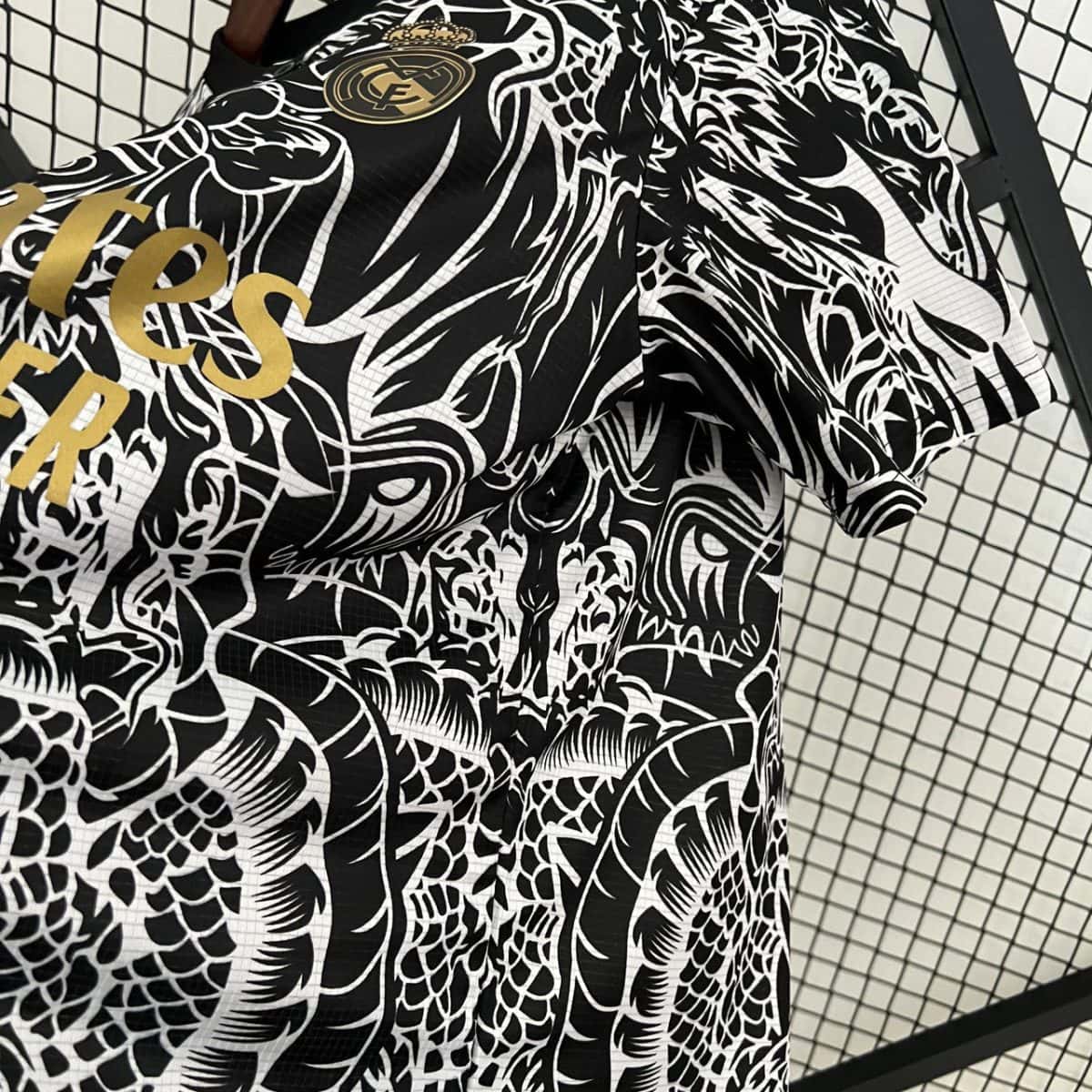 Close-up of a black-and-white dragon-pattern blazer with gold lettering and a gold circular crest on the chest, hanging in front of a chain-link fence.