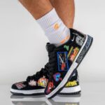 Black sneaker covered in colorful embroidered patches worn with white crew socks; urban streetwear style.