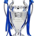 Silver trophy cup with blue ribbons draped from its handles on a white background.