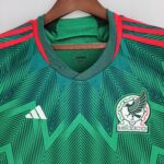 Close-up of a green Mexico soccer jersey on a hanger, showing the Adidas logo and national crest partially visible on the right side.