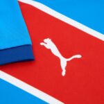 6240fcd7-6ab7-40f6-8028-ae2fd0d46401 | UAE SPORT STORE Close-up of a white Puma cat logo on a red jersey with blue fabric nearby, highlighting the brand symbol.