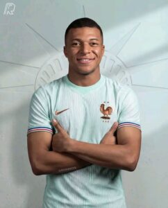Portrait of a smiling man with arms crossed, wearing a light blue France national team jersey with a rooster crest.