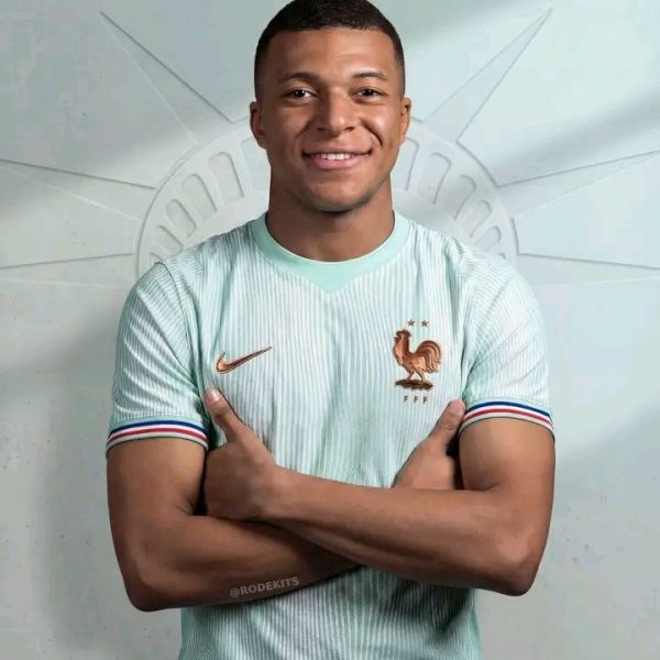 Portrait of a smiling man with arms crossed, wearing a light blue France national team jersey with a rooster crest.