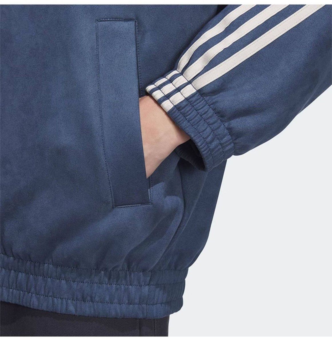 625fec97-1416-4a3f-9bb5-aa33f52ff762 | UAE SPORT STORE Close-up of a navy blue athletic jacket with white striped sleeves and a hand in the side pocket.