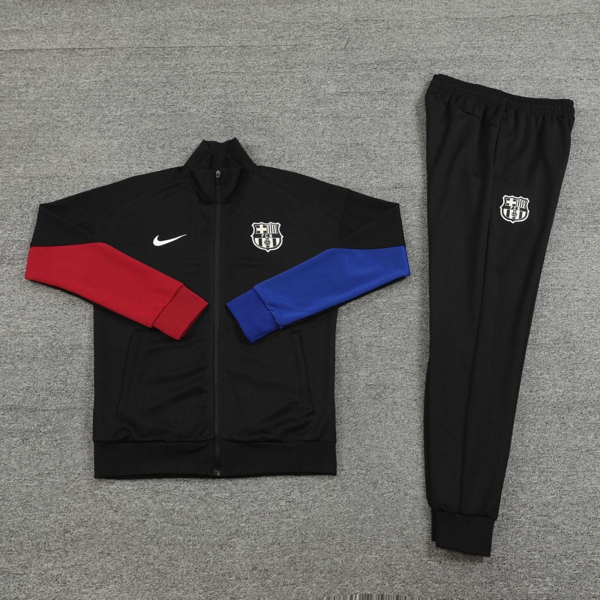 Black athletic jacket with red left sleeve and blue diagonal stripe, and a white crest on the chest, laid on a gray carpeted surface.