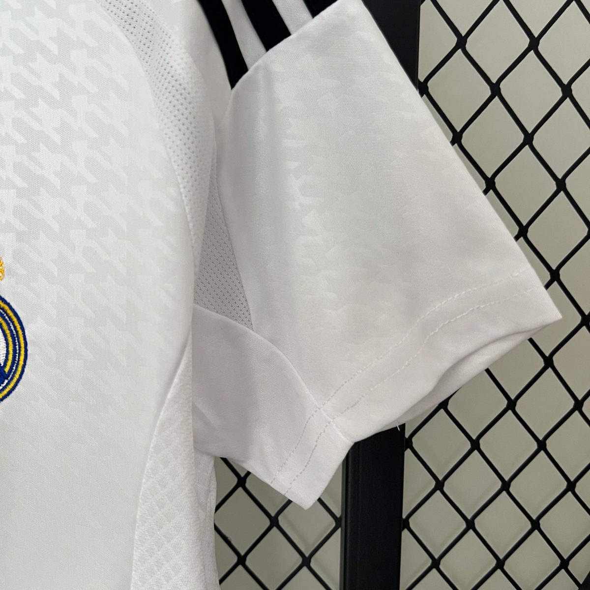 Close-up of white fabric with stitching, a gray seam running down the center, and a black metal post with a chain-link fence in the background.