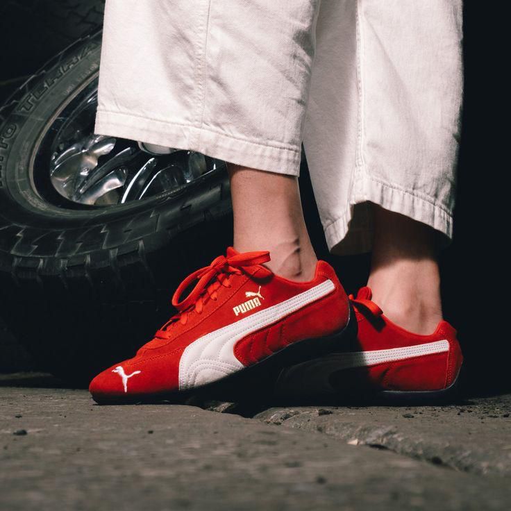 62f9a22d-e0c4-4ebc-bf1a-af2ca32cf350 | UAE SPORT STORE Person wearing red Puma sneakers with white stripes standing near a car tire.
