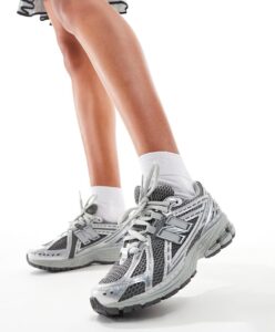 Gray athletic running shoes on feet in mid-step, white socks, white background (product photo).