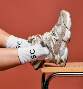 635b70d7-2400-4edf-9c1e-31eae299eb56_ab55a523-2f6c-4c1a-a606-43b45745be73 | UAE SPORT STORE Beige chunky sneakers and white ribbed socks resting on a wooden desk against an orange background.