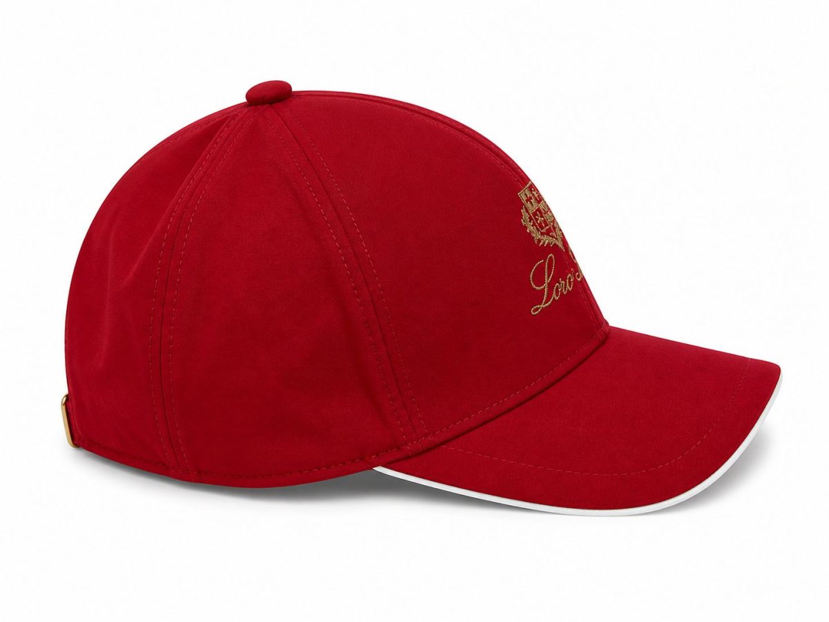 Red baseball cap with a curved brim, gold crest embroidery on the front, and a small back strap with a metal buckle.
