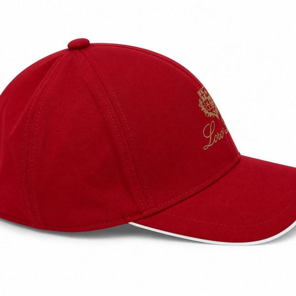 Red baseball cap with a curved brim, gold crest embroidery on the front, and a small back strap with a metal buckle.