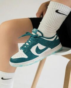 Teal and white Nike sneaker with white swoosh, worn with ribbed white socks, resting on a chair leg.