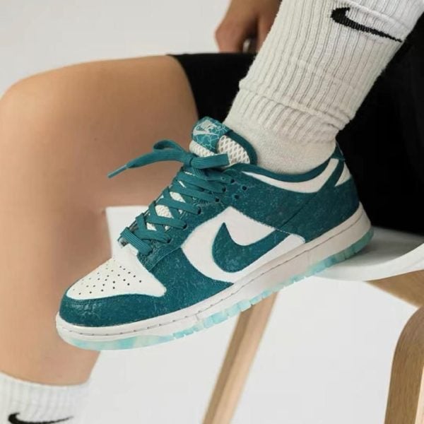 Teal and white Nike sneaker with white swoosh, worn with ribbed white socks, resting on a chair leg.