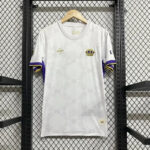 White athletic jersey with purple and gold sleeve trim, crown crest on the chest, hanging on a wooden hanger against a metal grid backdrop.