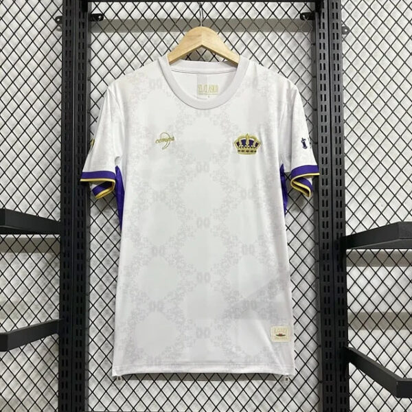 White athletic jersey with purple and gold sleeve trim, crown crest on the chest, hanging on a wooden hanger against a metal grid backdrop.