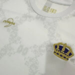 Close-up of a white shirt with a subtle gray damask pattern and a gold crown patch on the chest.