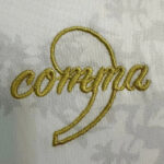 Close-up of gold cursive embroidery spelling 'compra' on white fabric.