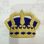 Embroidered gold crown patch with blue details on white fabric, decorative emblem style