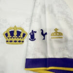 Embroidered white cloth with a gold crown on the left, blue symbols in the center, and a gold decorative emblem on the right, purple-yellow trim at the bottom edge.