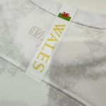 Close-up of a white fabric with a tag reading WALES in gold letters; a small Welsh flag (red dragon) sits at the top of the tag.