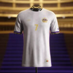 White soccer jersey on a stand with gold number 7 and crown crest, purple-trim sleeves, displayed in a stadium setting.