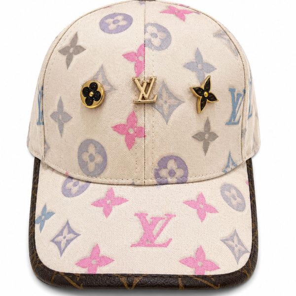 Beige Louis Vuitton baseball cap with multicolor LV monogram and gold emblem pins on the front rail.
