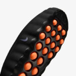 Close-up of a black football boot outsole with orange studs and a small Nike swoosh logo visible on the side.