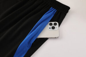 Black athletic pants with a blue side stripe, a smartphone tucked partially into the pocket nearby the waistband, visible camera module showing three lenses and flash.